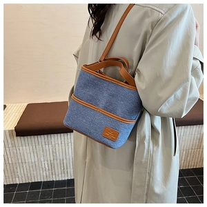 Détail du sac seau en denim bleu avec anses en cuir marron porté sur un manteau beige