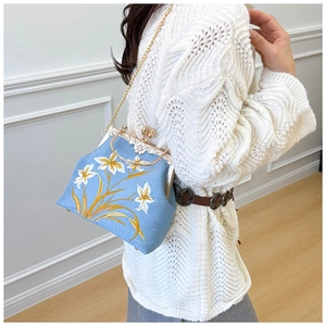 Detail of light blue canvas bag with white lily embroidery and gold chain strap