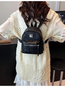 Modern black mini backpack with white polka dots worn by a female model in an indoor setting