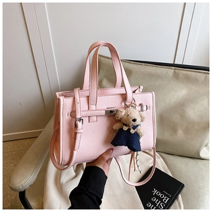 Detail of pink lychee leather handbag with metal turn-lock and cute teddy bear charm