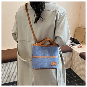 Détail d'un sac seau en denim bleu avec garniture en cuir brun porté par un mannequin