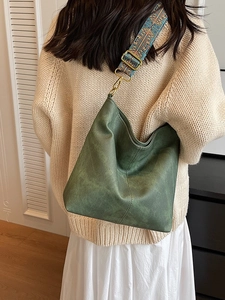 Dark green matte leather hobo bag with a colorful ethnic embroidery strap on beige sweater