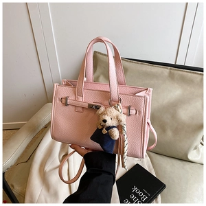 Detail of pink pebbled leather handbag featuring metal lock, silk scarf and bear charm