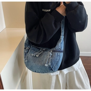 Detail of blue denim crescent hobo bag with fringe zippers worn by a model in casual style