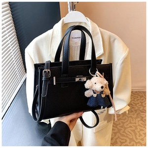 Detail of black litchi leather handbag with silver lock and teddy bear charm accessory