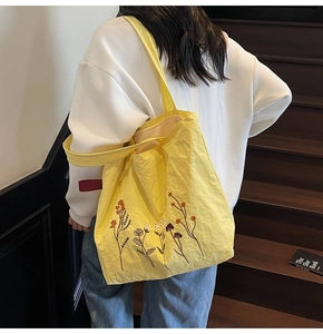 Close-up of yellow tote bag with floral embroidery on light pleated fabric