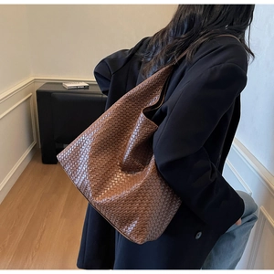 Brown woven leather tote bag showcased on a model shoulder in a minimalist interior