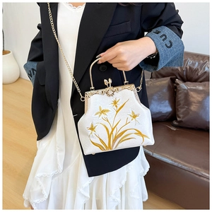 Detail of floral embroidery and gold metal frame on an ivory fabric crossbody bag