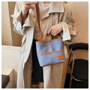 Sac seau en toile bleue avec garniture en cuir marron porté par un mannequin en intérieur