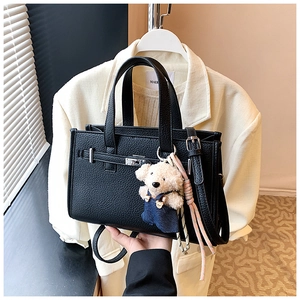 Close-up of black lychee grain leather handbag with silver lock and cute bear charm