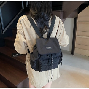 Close-up of black casual backpack with brand tag, wide straps, and woven drawstring detail