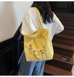 Detail of yellow tote bag featuring floral embroidery and textured nylon fabric on model
