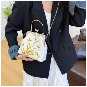 Detail of floral embroidery on white canvas handbag with gold clasp and chain strap