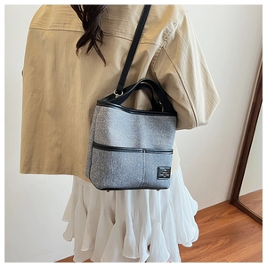 Détail du sac seau en tissu gris avec bordure en cuir noir et bandoulière porté par un mannequin