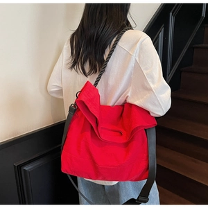 Detail of red canvas tote bag with black braided handles and adjustable nylon strap