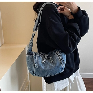 Blue denim crescent bag with tassel zipper details and adjustable strap on a model