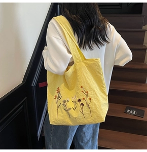 Detail of yellow tote bag featuring colorful floral embroidery and wide shoulder strap