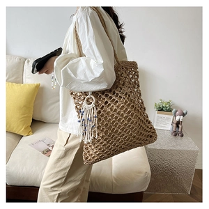 Close-up of hollow out woven straw tote bag with beaded tassel detail on shoulder strap
