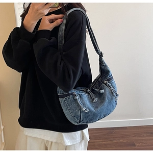 Detail of blue denim crescent bag with multiple zipper pockets and fringe tassels