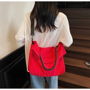 Detail view of large red nylon tote bag with black woven handles and wide strap