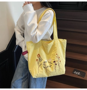 Detail of yellow nylon tote bag featuring colorful floral embroidery and purple strap