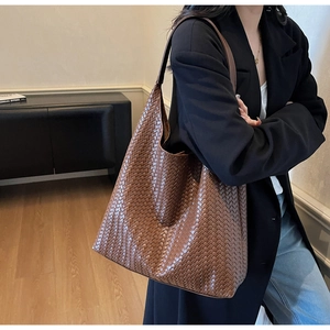 Detail of a brown woven leather tote bag with Intrecciato texture on a female model