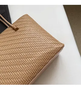 Detailed close-up of woven straw tote bag handle attachment and khaki braided texture