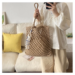 Close-up of large capacity hollow woven beach tote bag with a white tassel pendant detail