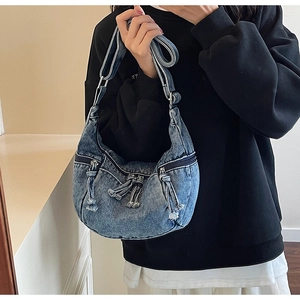 Detail view of washed denim moon bag featuring metal zippers and adjustable wide strap