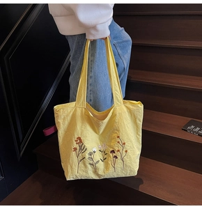 Detail of yellow nylon tote bag with floral embroidery and pink decorative tag
