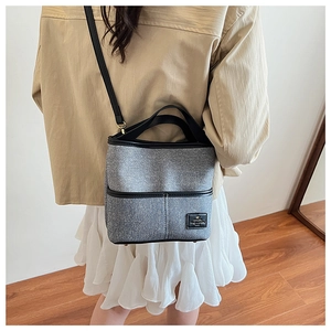 Détail du sac seau gris avec garniture en cuir noir porté par un mannequin à l'épaule