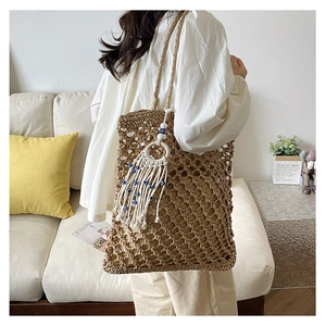 Detail of hollow woven straw tote bag featuring bohemian tassel with evil eye beads