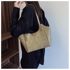Model wearing a large beige woven tote bag with brown leather straps in an indoor setting