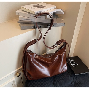 Detail of dark brown leather tote bag showing shiny texture and adjustable strap buckle