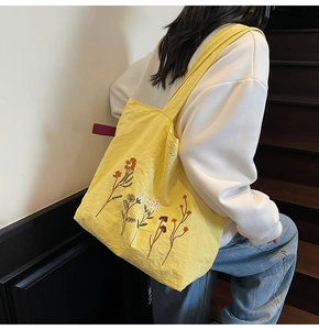 Close-up of bright yellow tote bag featuring colorful floral embroidery and nylon texture