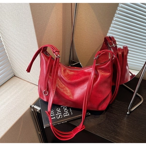 Detail of red soft leather tote bag with glossy texture and double straps on books