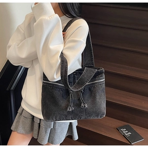 Detail of dark denim tote bag featuring decorative zippers and drawstring on a side-worn model