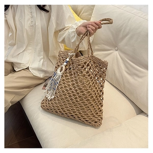 Detail of hollow woven straw beach tote bag featuring white tassels and blue bead accents
