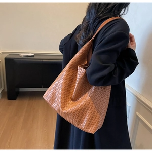 Detailed back view of a brown woven leather tote bag carried on a model shoulder