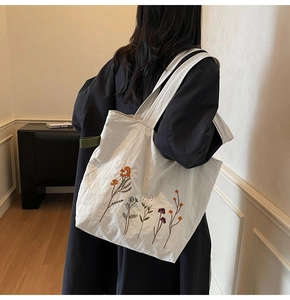 Detail showing colorful floral embroidery on white canvas tote bag with long shoulder strap