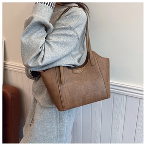 Brown woven tote bag with adjustable strap and metal logo plate shown on model
