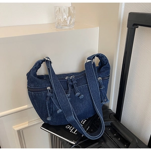 Detail of dark blue denim crescent bag with multi-zipper pockets and tassel pullers