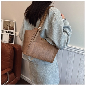 Brown woven texture tote bag with silver buckle worn by a model on a leather sofa