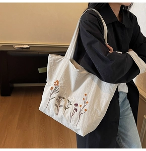 Close-up of a beige canvas tote bag featuring colorful floral embroidery on the shoulder strap