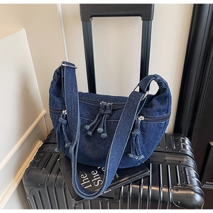 Detail of dark blue denim hobo bag on luggage showing adjustable strap and zip pockets