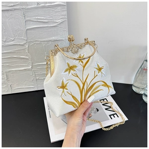 Detailed close-up of vintage floral embroidery and ornate golden metal frame on white handbag