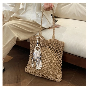 Detail of bohemian straw tote bag with intricate hollow weave and eye tassel charm