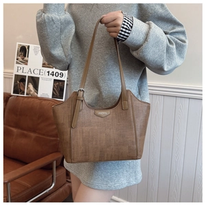 Close-up of brown tote bag with woven texture, leather logo tag, and adjustable strap