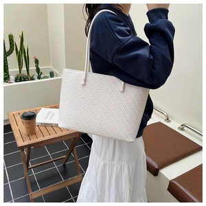 Detail of white woven tote bag with V-pattern texture and long shoulder strap in a cafe