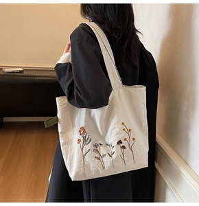 Detailed close-up of embroidered floral patterns on a beige canvas tote bag